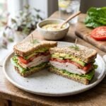 Healthy turkey sandwich with whole-grain bread, sliced turkey, lettuce, tomato, cucumber, avocado, and creamy yogurt spread